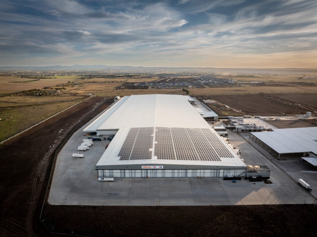 Rectangular warehouse facility at sunset featuring a white roof partially covered in solar panels