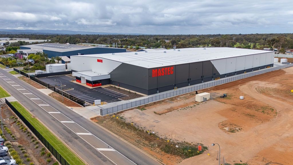 An aerial view of a large, modern industrial warehouse with "MASTEC" in red lettering on the side