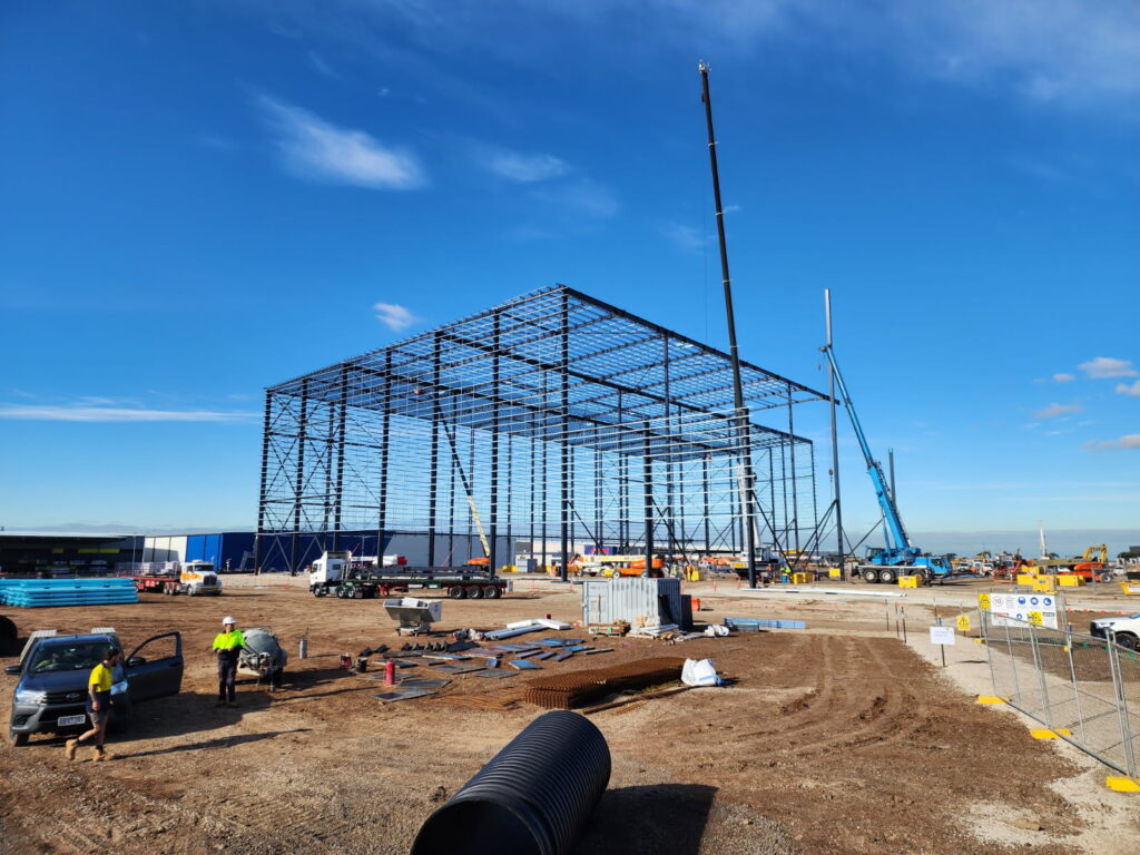 A large steel warehouse frame under construction against a clear blue sky