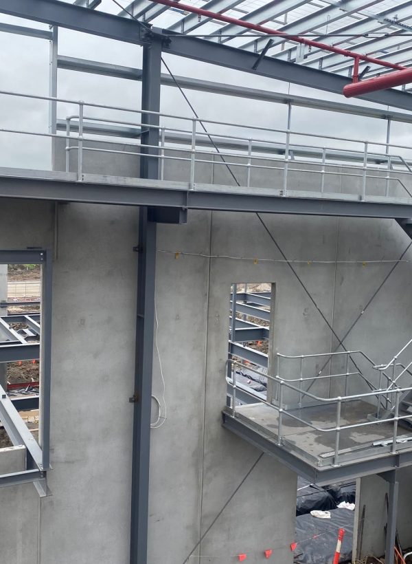An exterior view of a multi-level steel staircase and landing attached to a concrete industrial building under construction