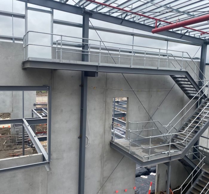 An exterior view of a multi-level steel staircase and landing attached to a concrete industrial building under construction