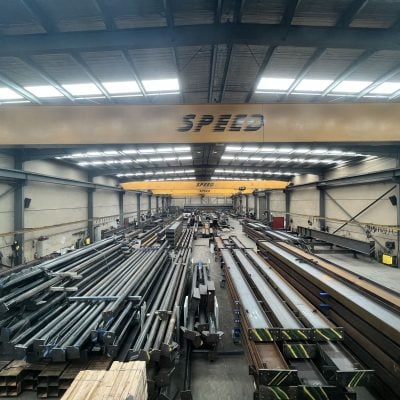 A large industrial steel fabrication warehouse filled with organised stacks of metal beams and columns.